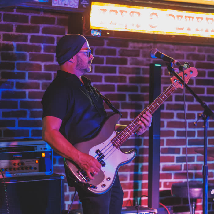 Leo de Menezes on bass against the brick back wall